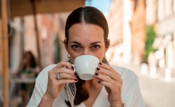 A woman sipping on a cup of coffee while staring straight at the camera